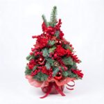 „Świąteczna dekoracja w formie choinki ozdobiona czerwonymi różami, bombkami i jagodami – produkt od kwiaciarni Kwiatowe Królestwo.”Kwiaty Warszawa